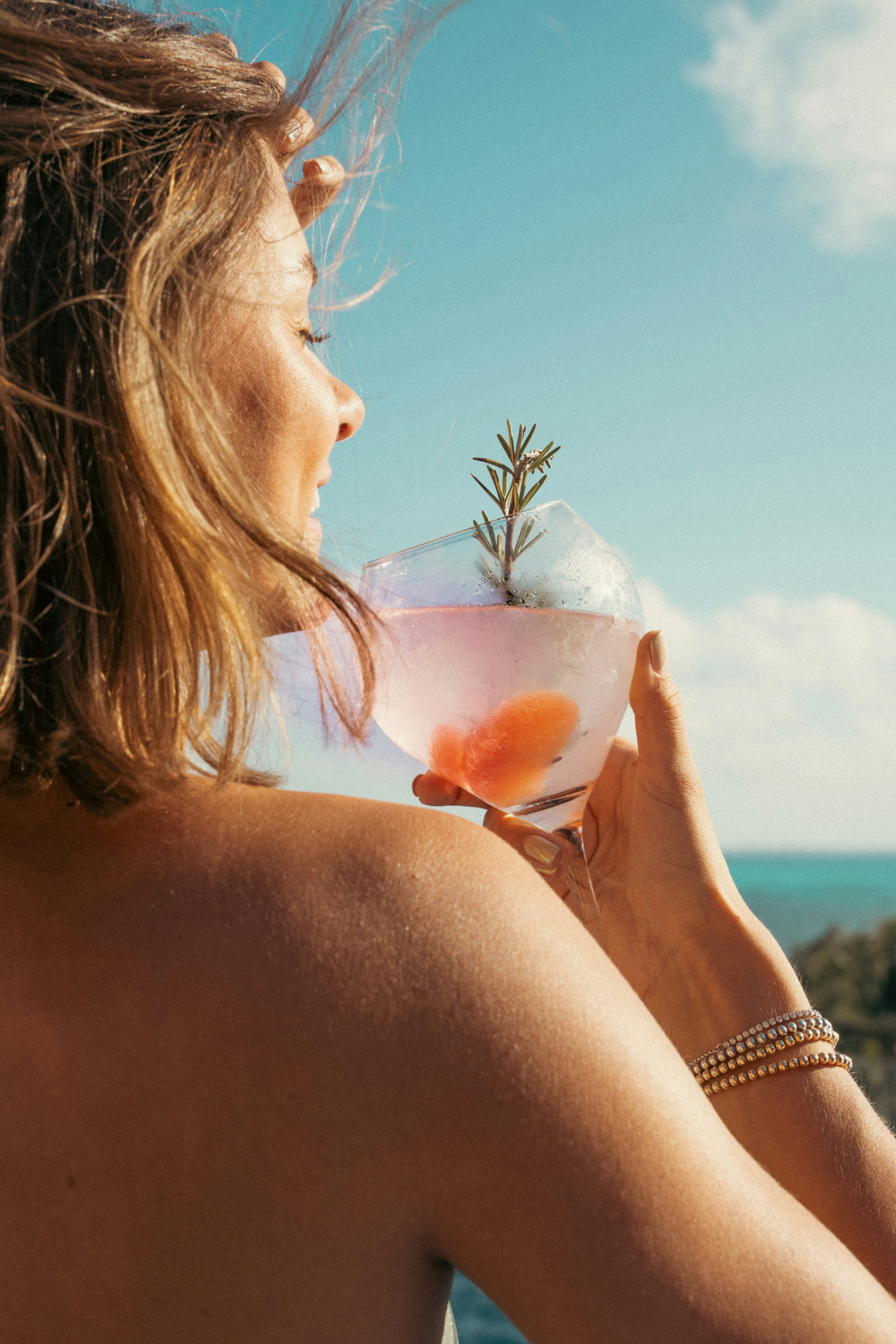 A guest holds a rosemary-garnished cocktail against the Aegean sky.